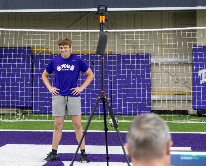 A TCU Football player stands near a soccer goal inside the Sam Baugh Indoor Practice Facility, with several Go Pro cameras surrounding him, tracking his body movement to collect data.
